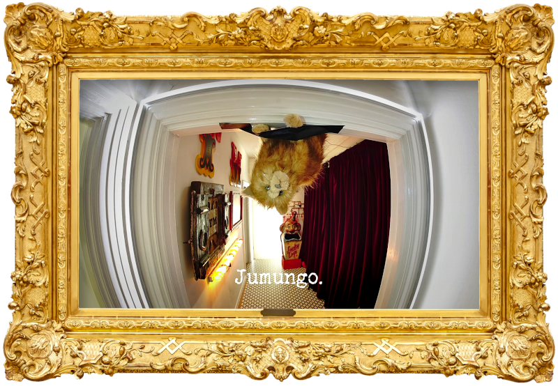 Photo of Patatas, the plush cat toy, gaffer-taped upside-down to a doorframe in the hallway of the Taskmaster house (referencing the 'The most fun thing to turn upside-down', 'Rescue Patatas from the dome', and potentially also the 'Stick the heaviest thing to the board' tasks), with the episode title, 'Jumungo', superimposed on it.