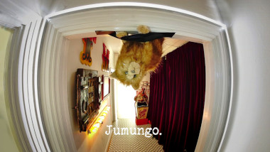 Photo of Patatas, the plush cat toy, gaffer-taped upside-down to a doorframe in the hallway of the Taskmaster house (referencing the 'The most fun thing to turn upside-down', 'Rescue Patatas from the dome', and potentially also the 'Stick the heaviest thing to the board' tasks), with the episode title, 'Jumungo', superimposed on it.