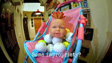 Photo of a baby doll head with a  succulent in the top of it, balanced on top of a pile of golf balls, in a pink and blue push-chair, in the hallway of the Taskmaster house (referencing the baby in the 'Complete the jobstacle course' and the golf caddy in the 'Work out who is following you' tasks), with the episode title, 'Some impropriety?', superimposed on it.