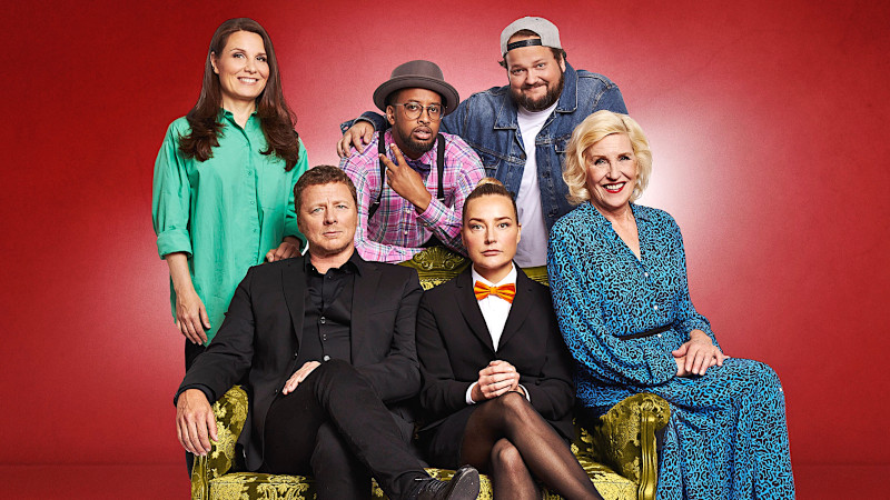 Image depicting the hosts and fixed contestants for season 4 of Suurmestari, seated on and gathered around a sofa.