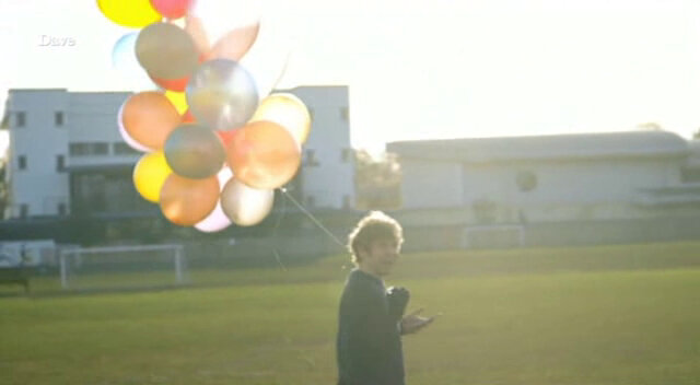 Backlit image of Josh Widdicombe holding a bunch of balloons in the middle of a football pitch, while creating his drawing using a GPS device.