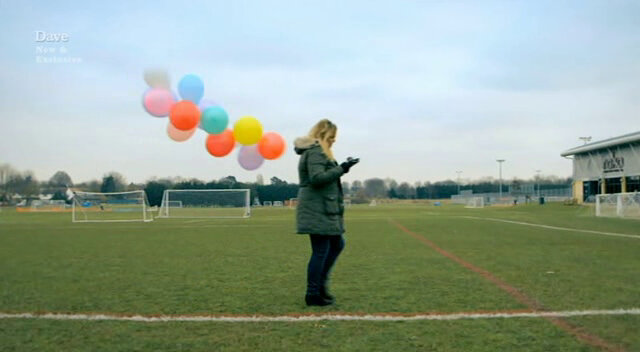 Image of Roisin Conaty holding a bunch of balloons in the middle of a football pitch, while creating her drawing using a GPS device.