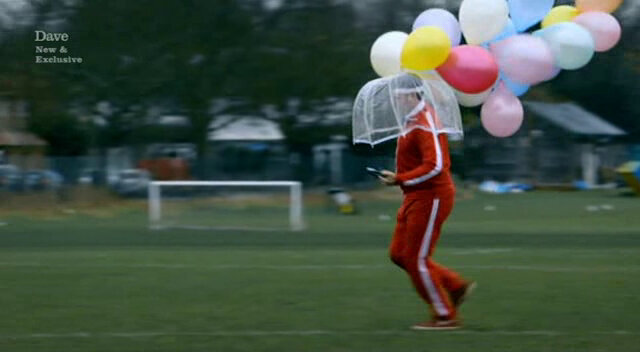 Image of Tim Key running across a football pitch in the torrential rain, holding a transparent umbrella and a bunch of balloons, as he tries to create a drawing using a GPS device.