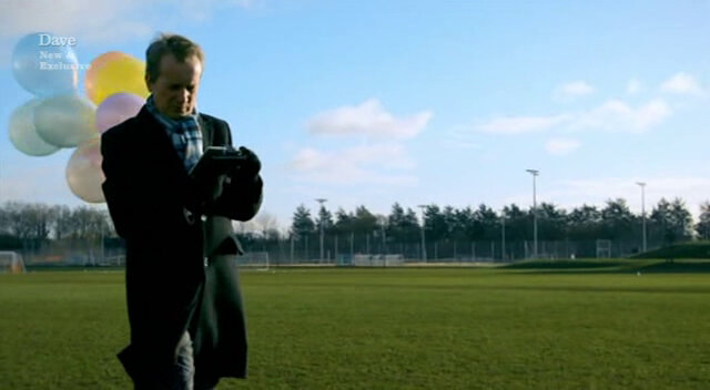 Image of Frank standing in the middle of a football pitch, holding a bunch of balloons, as he tries to create a drawing using a GPS device.