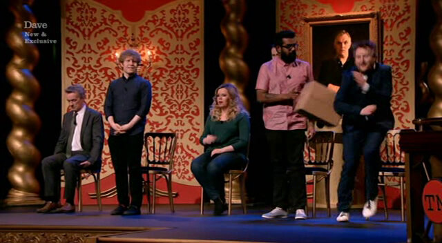 Image of Romesh attacking Tim with his cardboard box for standing up at the same time as him.