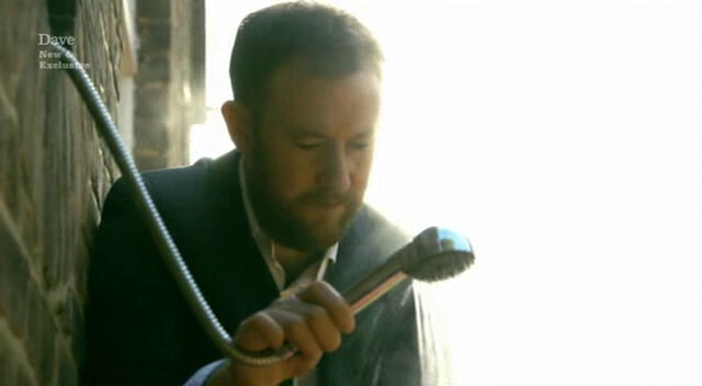 Image of Alex Horne performing the function of Roisin Conaty’s shower head holder.