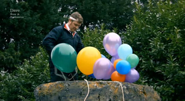 Image of Tim Key giving up on his genius plan to float the boulder away using helium balloons.