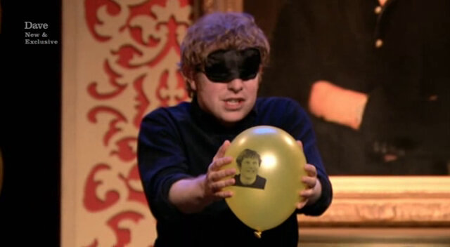 Image of Josh Widdicombe anxiously holding out his inflated balloon while still blindfolded.