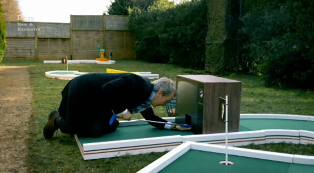 Image showing Frank Skinner adopting a snooker technique to get his egg through the TV tunnel obstacle of the ‘R’-shaped mini golf hole.