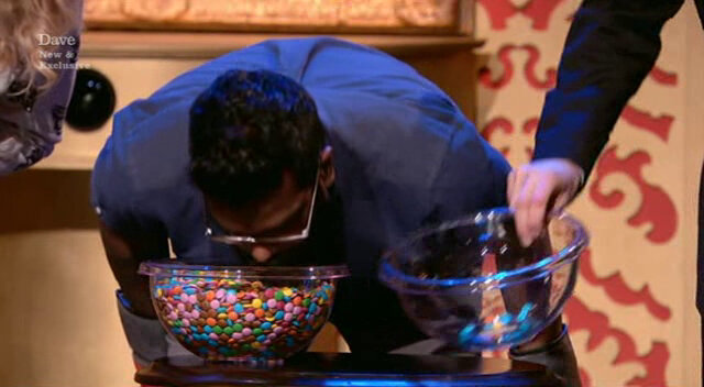 Image of Romesh Ranganathan with his face in a bowl of Smarties, semi-blindly trying to extract the blue ones with his mouth.