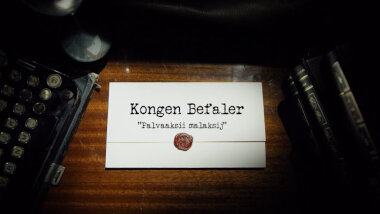 Image of the title card at the start of this episode, showing a task brief with the show title, 'Kongen Befaler', and the episode title, 'Palvaaksii malaksij' [made-up Finnish], on a wooden desk. At the edges of the image, part of a typewriter keyboard and a stack of leather-bound books can be seen.