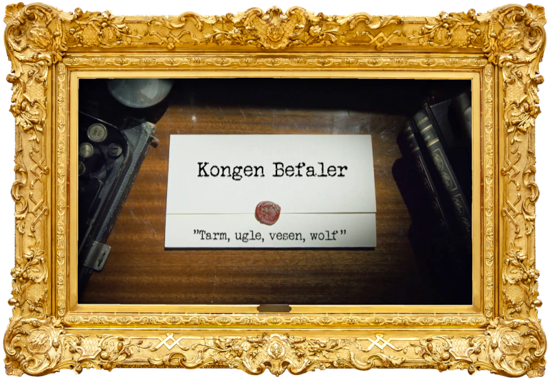Image of the title card at the start of this episode, showing a task brief with the show title, 'Kongen Befaler', and the episode title, 'Tarm, ugle, vesen, wolf' ['Intestine, owl, creature, wolf'], on a wooden desk. At the edges of the image, part of a typewriter keyboard and a stack of leather-bound books can be seen.