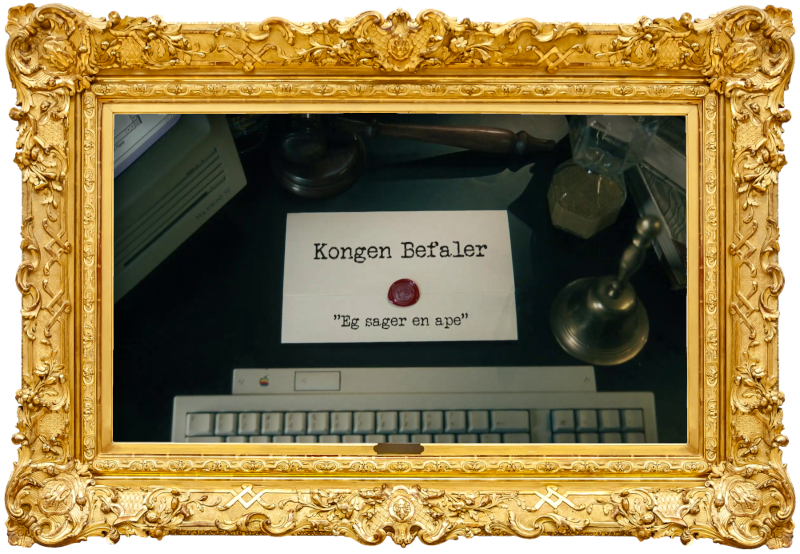 Image of the title card at the start of this episode, showing a task brief with the show title, 'Kongen Befaler', and the episode title, 'Eg sager en ape' ['I'm sawing a monkey'], on a wooden desk. Also on the desk is an old-fashioned Apple computer and keyboard, a gavel, an hourglass, and a bell.