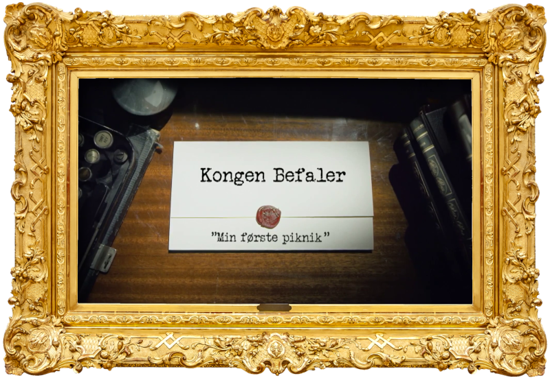Image of the title card at the start of this episode, showing a task brief with the show title, 'Kongen Befaler', and the episode title, 'Min første piknik' ['My first picnic'], on a wooden desk. At the edges of the image, part of a typewriter keyboard and a stack of leather-bound books can be seen.