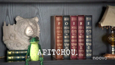 Image of a bookshelf upon which there is a whiten ceramic sculpture of a bear, a green wooden frog, a group of five books with the letters 'P', 'O', 'I', 'R', and 'E' on their spines, and a small ornate lamp with a lampshade (it's unclear what this image might be a reference to), with the episode title, 'Apitchou' ['Achoo'], superimposed on it.