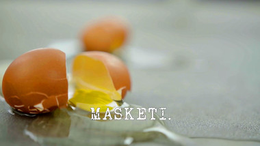 Image of a broken egg on the floor (a reference to the 'Remove the napkin from underneath the eggs' task), with the episode title, 'Masketi', superimposed on it.