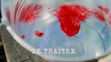 Image of a red Jell-O cup at the bottom of a metal bucket (a reference to the 'Eat one item, balance one item, throw one item' task), with the episode title, 'Le traître' ['The traitor'], superimposed on it.
