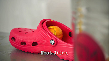 Image of a red croc with some orange peel inside of it (a reference to the 'Fill the glass with orange juice' task), with the episode title, 'Foot juice', superimposed on it.