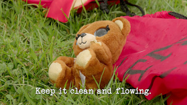 Image of a teddy bear laid on some grass, in front of a red nylon bag (a reference to the 'Let the cat out of the bag' task), with the episode title, 'Keep it clean and flowing', superimposed on it.