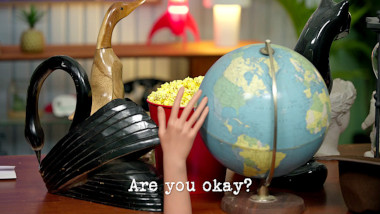 Image of a bucket of popcorn on a desk, surrounded by figurines of birds and cats, a mannequin's hand, and a world globe (a reference to the 'Protect the popcorn' task), with the episode title, 'Are you okay?', superimposed on it.