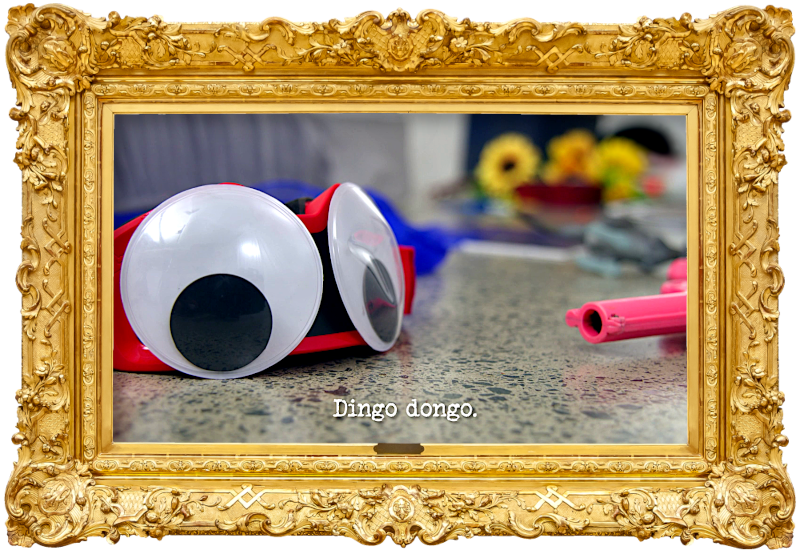 Close-up image of some goggles with large googly eyes stuck to them, laid on the floor of the lab, with an assortment of other items including a pink toy gun (a reference to Anne Edmonds' and Josh Thomas' attempt at the 'Correctly identify items through a mattress' task), with the episode title, 'Dingo dongo', superimposed on it.