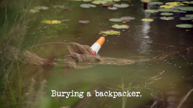 Image of a traffic cone submerged in a pond (a reference to Rhys Nicholson's attempt at the 'Hide 10 traffic cones from Tom' task), with the episode title, 'Burying a backpacker', superimposed on it.