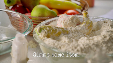 Image of some flour paste covered fruit in a bowl of flour (a reference to the ‘Glue an item to the ceiling of the caravan’ task), with the episode title, ‘Gimme some item’, superimposed on it.