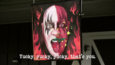Image of Tom Gleeson's portrait, painted in the style of an album cover from the band Kiss, hanging from the balcony of those house, with splatters of green and yellow paint on it (a reference to Dave Hughes' and Lisa McCune's attempt at the 'Charge!' task), with the episode title 'Yucky, yucky, yucky, that’s you' superimposed on it.