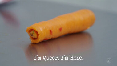 Image of a hollowed out carrot with part of a brussels sprout poking out of it (a reference to the 'Hide a vegetable completely inside another' task), with the episode title, 'I'm queer, I'm here', superimposed on it.