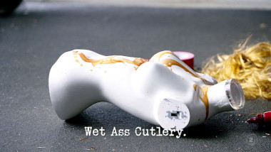 Image of a female mannequin's torso, covered in tomato ketchup, lying on the ground (a reference to the 'Trick or treat Paul' task), with the episode title, 'Wet Ass Cutlery', superimposed on it.