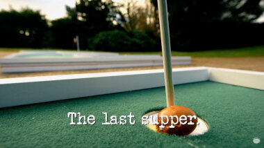 Image of an egg resting against the flagpole of a mini golf course hole (taken from the 'Play mini golf with eggs' task), with the episode title, ‘The last supper’ superimposed on it.