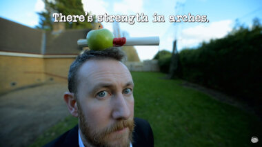 Image of Alex Horne with an apple balanced on his head, through which a rolled-up task brief has been inserted (it's unclear what this image is a reference to...), with the episode title, 'There’s strength in arches', superimposed on it.