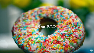 Image of a doughnut covered in icing and hundreds and thousands (a reference to the 'The lowest unique number of doughnuts' task), with the episode title, 'The F.I.P.', superimposed on it.