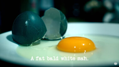 Image of a raw egg on a plate, along with the two halves of the black eggshell it came out of (it's unclear what this image is a reference to...), with the episode title, 'A fat bald white man', superimposed on it.