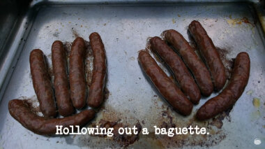 Image of ten cooked sausages on a baking tray, arranged in the form of two hands (presumably a reference to Greg calling Mel Giedroyc 'Sausage Gloves', after she put sausages inside her driving gloves during the 'Persuade three animals to stand on the mat' task), with the episode title, 'Hollowing out a baguette', superimposed on it.