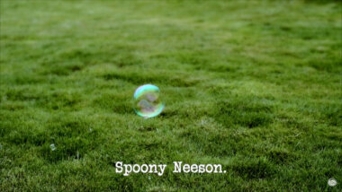 Image of a single soap bubble, floating above a lawn (a reference to the bubbles which appeared in the 'Light a candle using a cupcake' task), with the episode title, 'Spoony Neeson', superimposed on it.