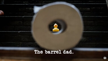 Image of a rubber duck, seen through the centre of a roll of toilet paper (presumably a combined reference to the 'Get the toilet paper through the toilet seat' and ducks used in the 'Make the best thing to entertain a toddler' tasks), with the episode title, 'The barrel dad', superimposed on it.