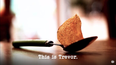 Image of a single crisp balanced on a spoon on a table (a reference to the 'Work out the crisp flavours' task), with the episode title, 'This is Trevor', superimposed on it.