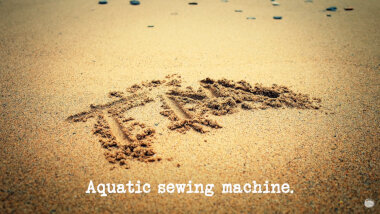Image of the letters 'TM' written in the sand of a beach (a reference to the 'Make a portrait of a former contestant using sand and one tool' task), with the episode title, 'Aquatic sewing machine', superimposed on it.