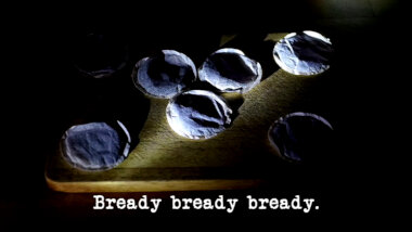 Image of six circular teabags on a wooden board, lit by a thin shaft of light (this does not seem to be a reference to anything that occurred during the episode), with the episode title, 'Bready bready bready', superimposed on it.