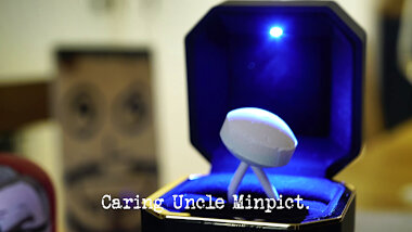 Image of a lollipop with its stick bent to make it into a ring, presented in a large ring box with an internal light (a reference to the 'Propose to Alex' task), with the episode title, 'Caring Uncle Minpict', superimposed on it.