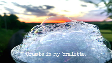 Image of a foam of soap bubbles against a sunset (a reference to the 'Turn on the bubble machine' task), with the episode title, 'Crumbs in my bralette', superimposed on it.