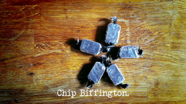 Image of five sweets arranged in a star shape on a wooden surface (a reference to John Kearns' attempt at the 'Get the most pleasure from these rubber chutes' task), with the episode title, 'Chip Biffington', superimposed on it.