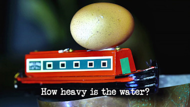 Photo of an egg balanced on top of a toy narrowboat (a reference to the 'Make the fastest egg boat' tasks), with the episode title, 'How heavy is the water?', superimposed on it.