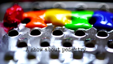 Close up photo of paint in rainbow colours on a metal cheese grater (a reference to the 'Make these things the same colour' and 'Make exactly 99 holes in the piece of paper' tasks), with the episode title, 'A show about pedantry', superimposed on it.