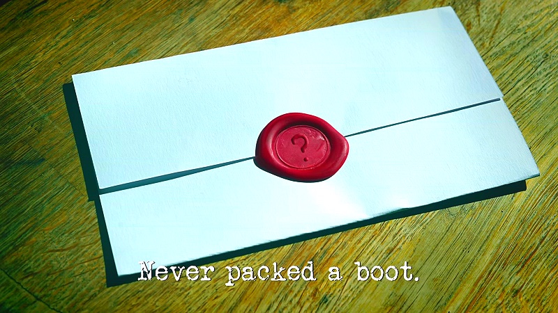 Photo of a task brief with a wax seal featuring a question mark, rather than the usual 'TM', laid on a wooden surface (a reference to the 'Find the secret task' task), with the episode title, 'Never packed a boot', superimposed on it.