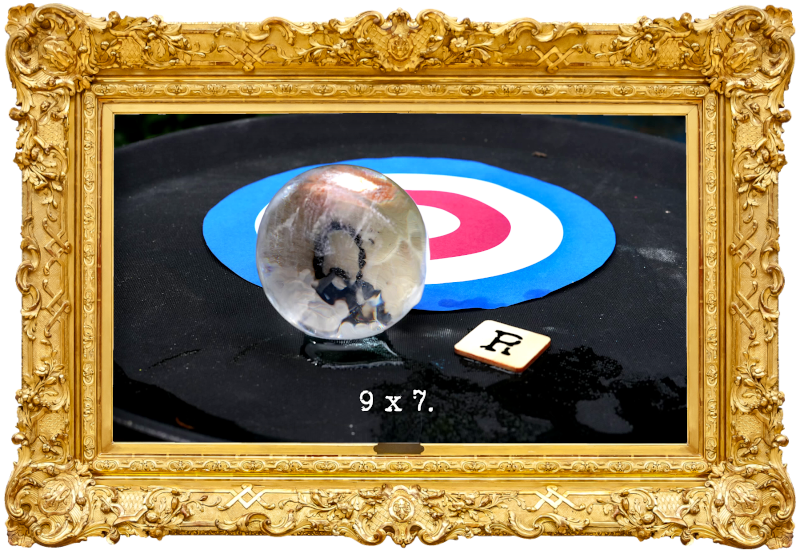 Photo of an ice ball with a letter 'Q' embedded within it, and a wooden tile with the letter 'R' printed on it, lying in front of a target consisting of concentric blue, white and red rings (referencing the 'Honk the horn' and 'Roll an object onto the target' tasks), with the episode title, '9 x 7', superimposed on it.