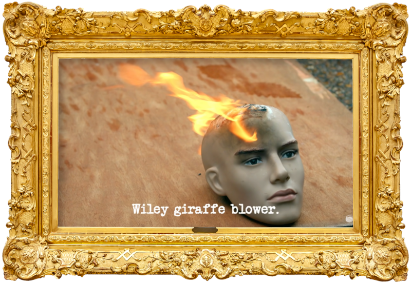 Image of a mannequin's head, set aflame, on top of a wooden board on the ground (taken during Bob Mortimer's attempt at the 'Perform a miracle' task), with the episode title, 'Wiley giraffe blower', superimposed on it.