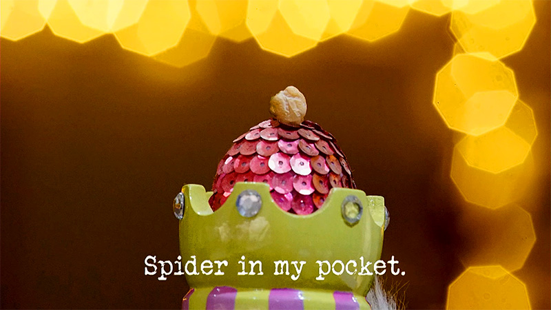 Photo of a colourful ceramic crown with a sequin-covered egg inside it, and a chickpea balanced on top (a reference to the 'Be the best waiter' and 'Get a hat onto the Taskmaster’s head' tasks), with the episode title, 'Spider in my pocket', superimposed on it.