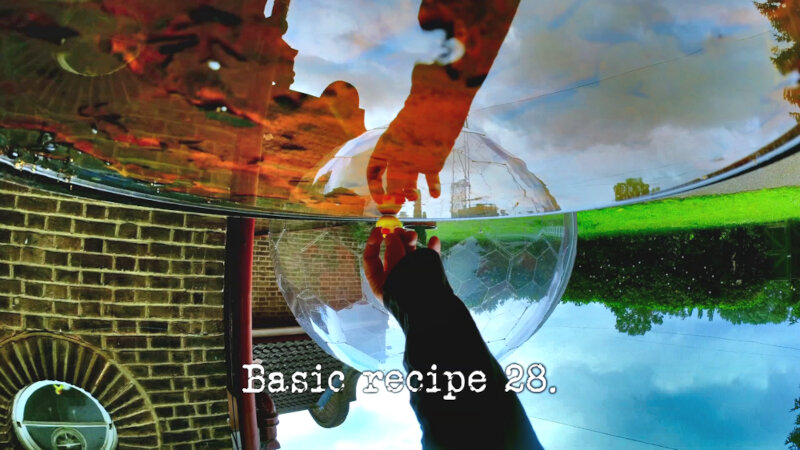 Upside-down image of the wet top surface of an oil drum, in which the reflection of an arm reaching for a small rubber duck can be seen, along with a reflection of the plastic dome (possibly a reference to the 'The most beguiling, unwieldy, shiny thing' task), with the episode title, 'Basic recipe 28', superimposed on it.